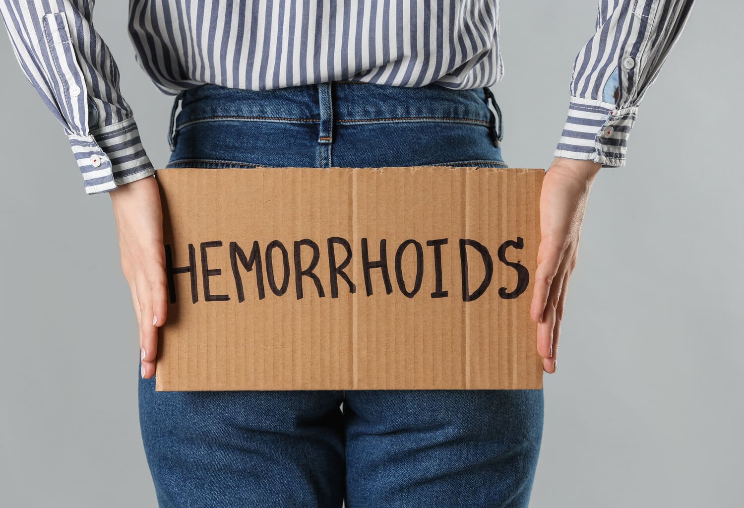 Woman,Holding,Carton,Sign,With,Word,Hemorrhoids,On,Light,Grey